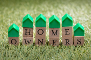 What are the benefits of an HOA? Miniature House Model Over Wooden Block Showing Home Owners Text On Green Grass